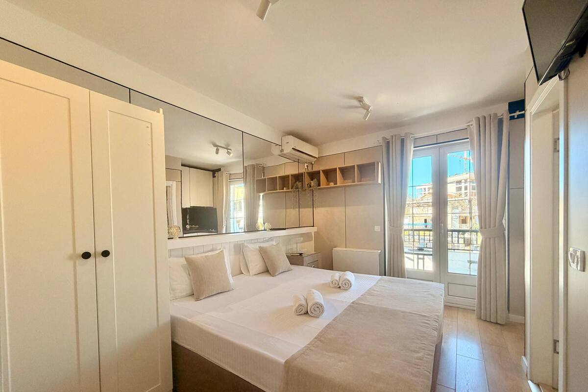 A hotel room with a large bed, a TV, a mirror, and a balcony with curtains.