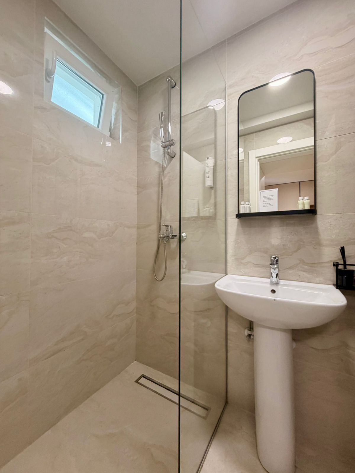 A modern bathroom with a glass-enclosed shower, a pedestal sink, and a mirror above the sink.
