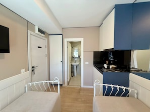 A compact room with a bed, a small kitchenette, and a bathroom visible through an open door.
