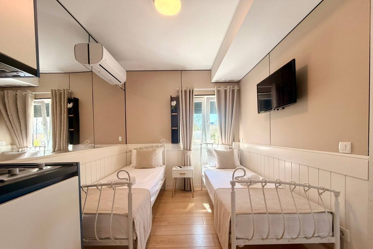 A room with two beds, a small table, a TV, and an air conditioning unit.