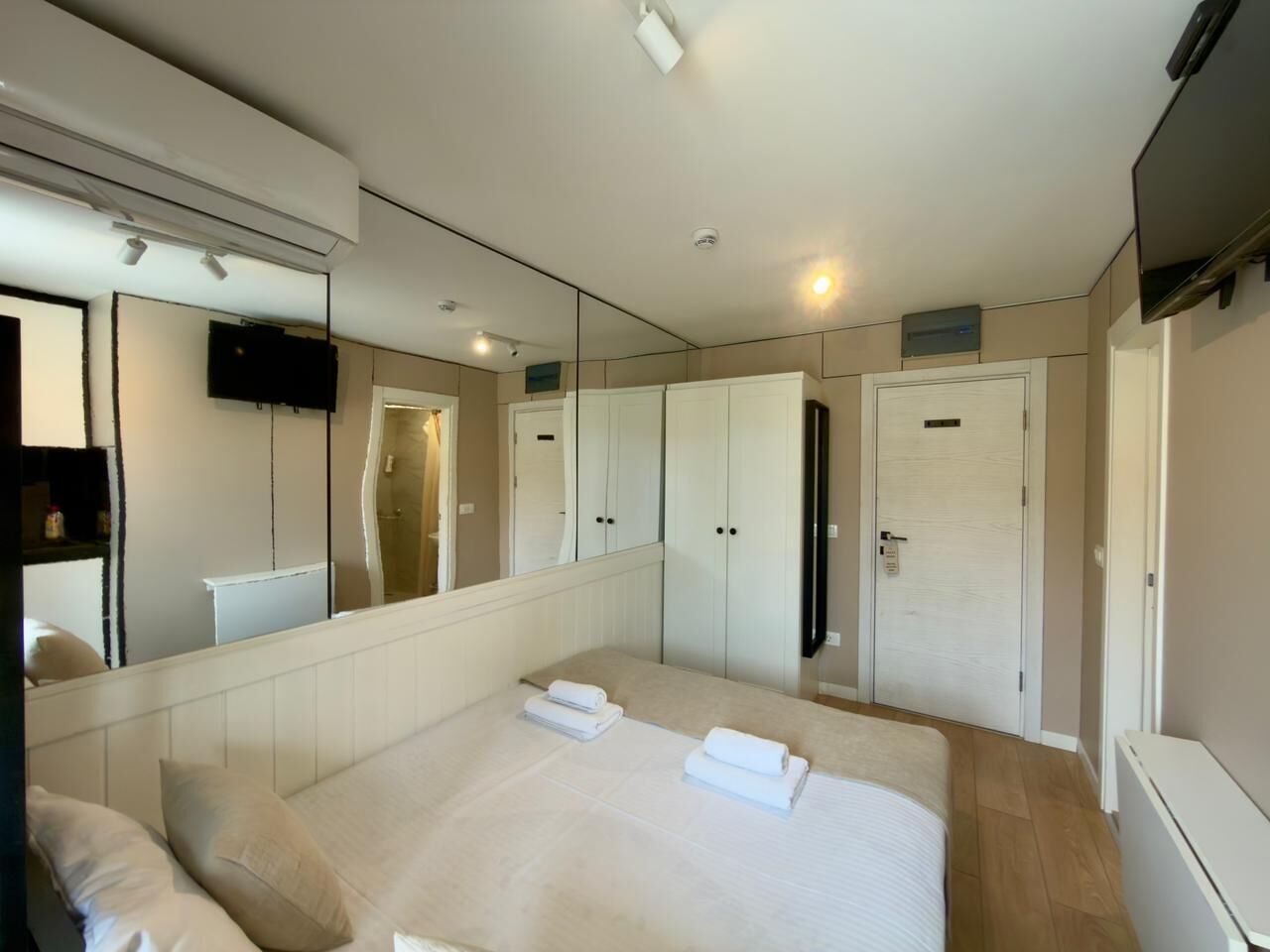 A bedroom with a large bed, a mirror, a TV, and a wardrobe.