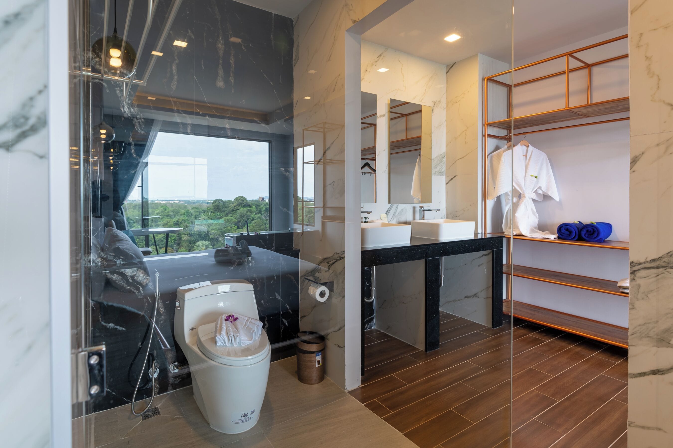 A modern bathroom with a marble vanity, a shower area, and a view of greenery outside.