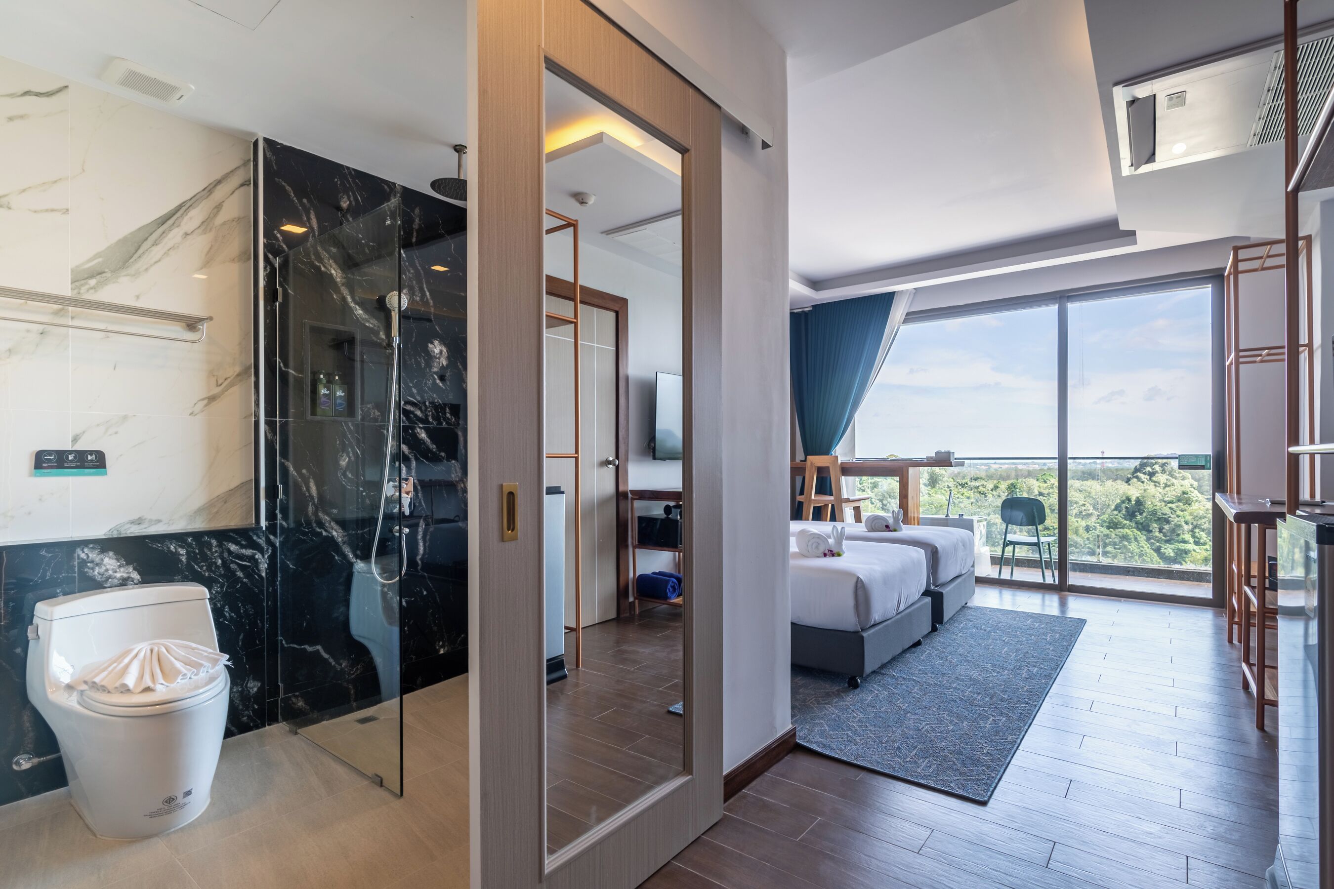 A modern hotel room with a marble bathroom, a large bed, a balcony with a view, and a TV.
