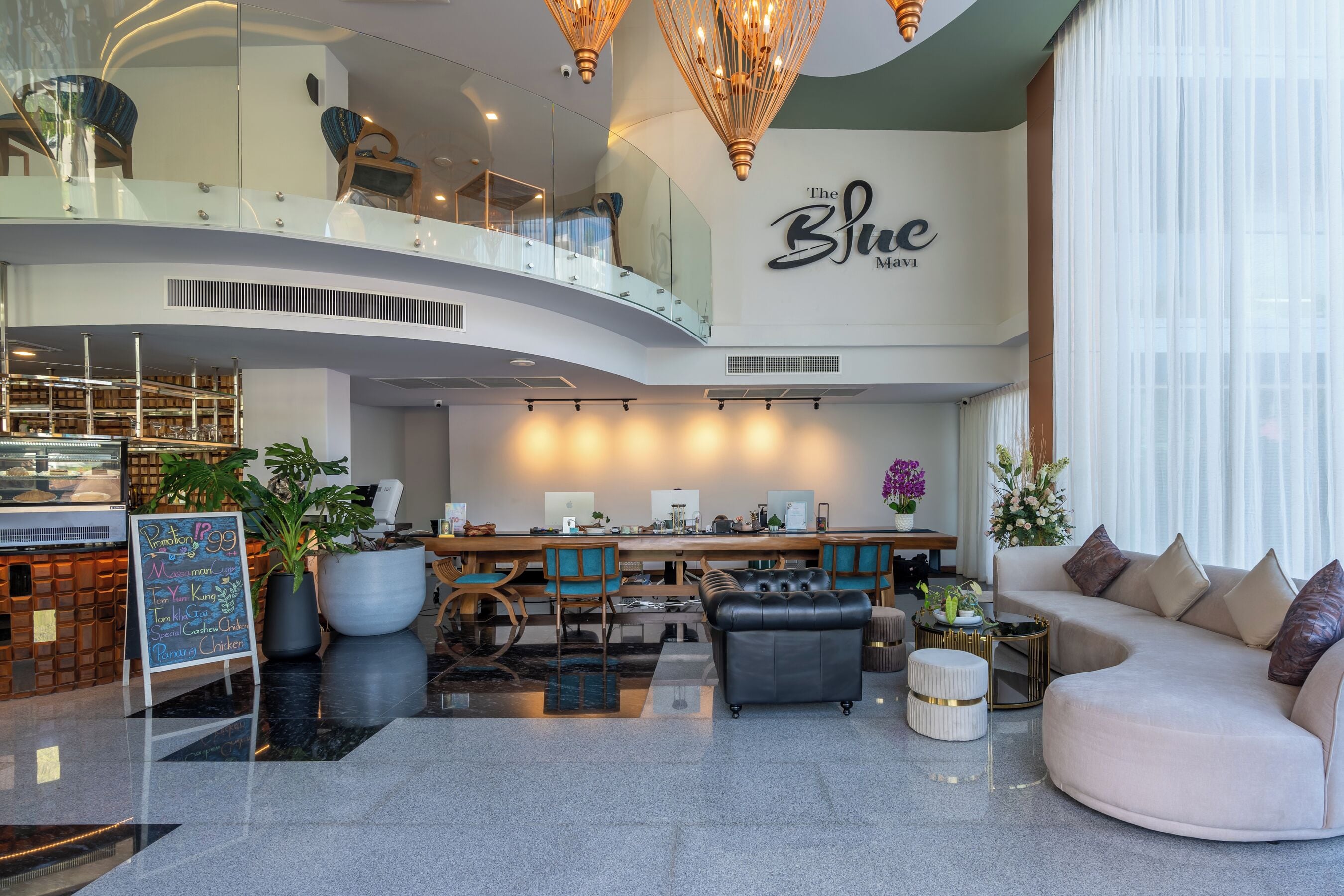 A modern hotel lobby with a curved staircase, a dining area, and a seating area with a sofa and chairs.