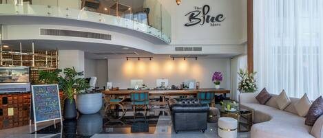 A modern hotel lobby with a curved staircase, a dining area, and a seating area with a sofa and chairs.