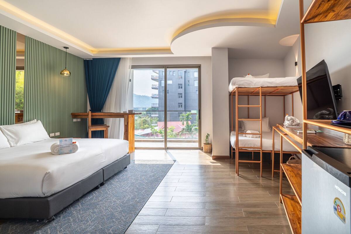 A modern hotel room with a large bed, a desk, a bunk bed, and a view of the city.