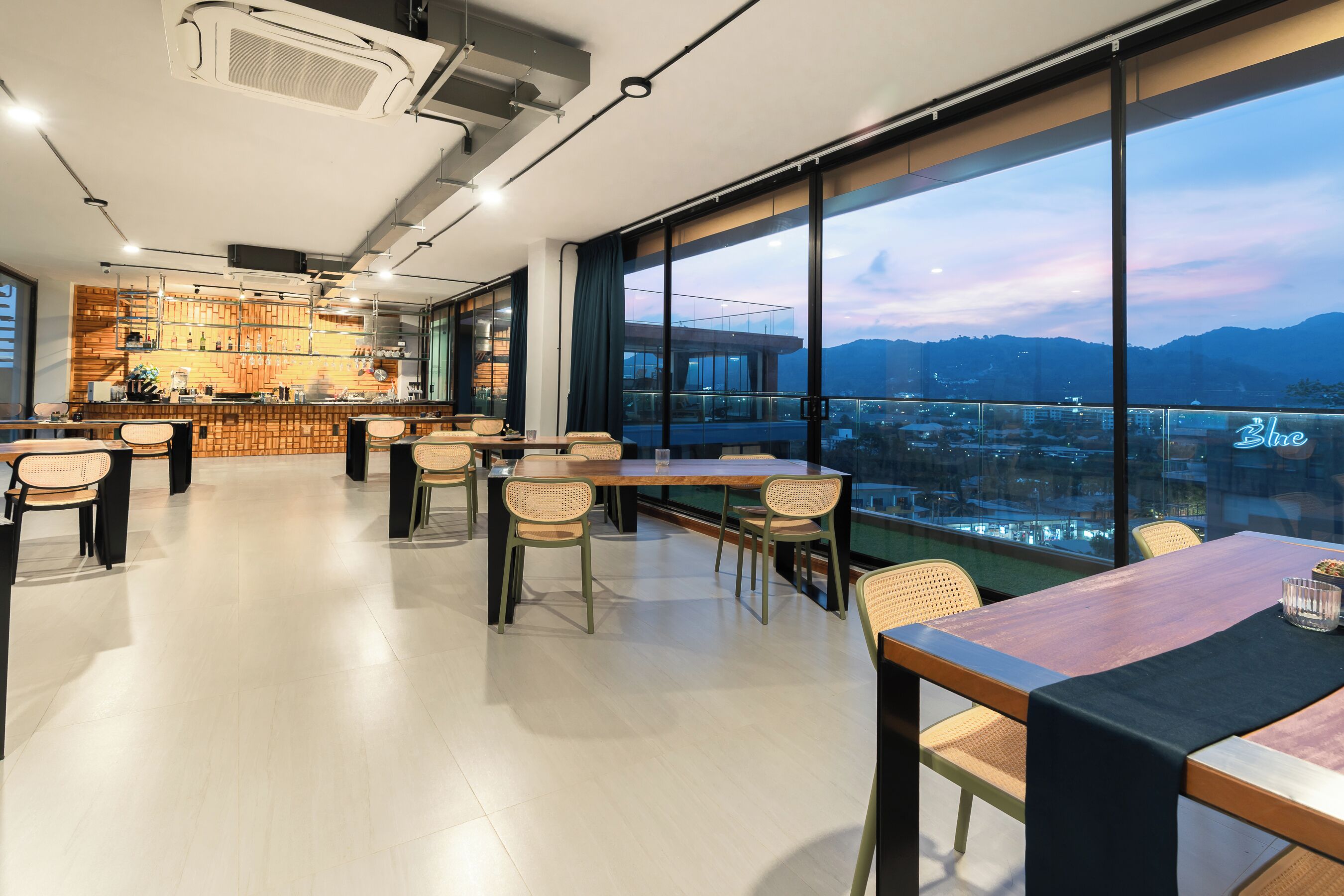 Un restaurante moderno con zona de bar, amplios ventanales que ofrecen vistas a la ciudad y una combinación de mobiliario de madera y metal.