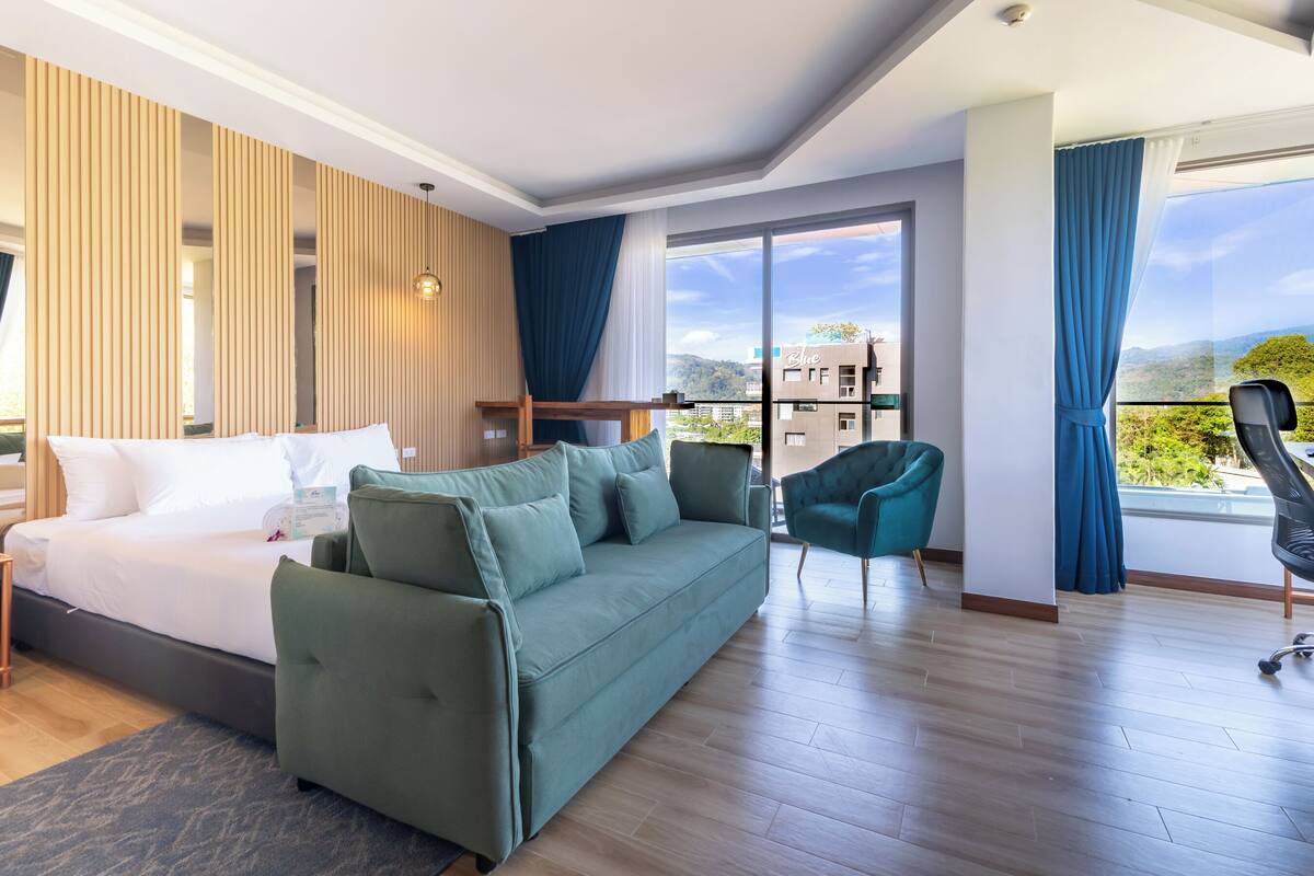A modern hotel room with a bed, green sofa, and a view of the city.