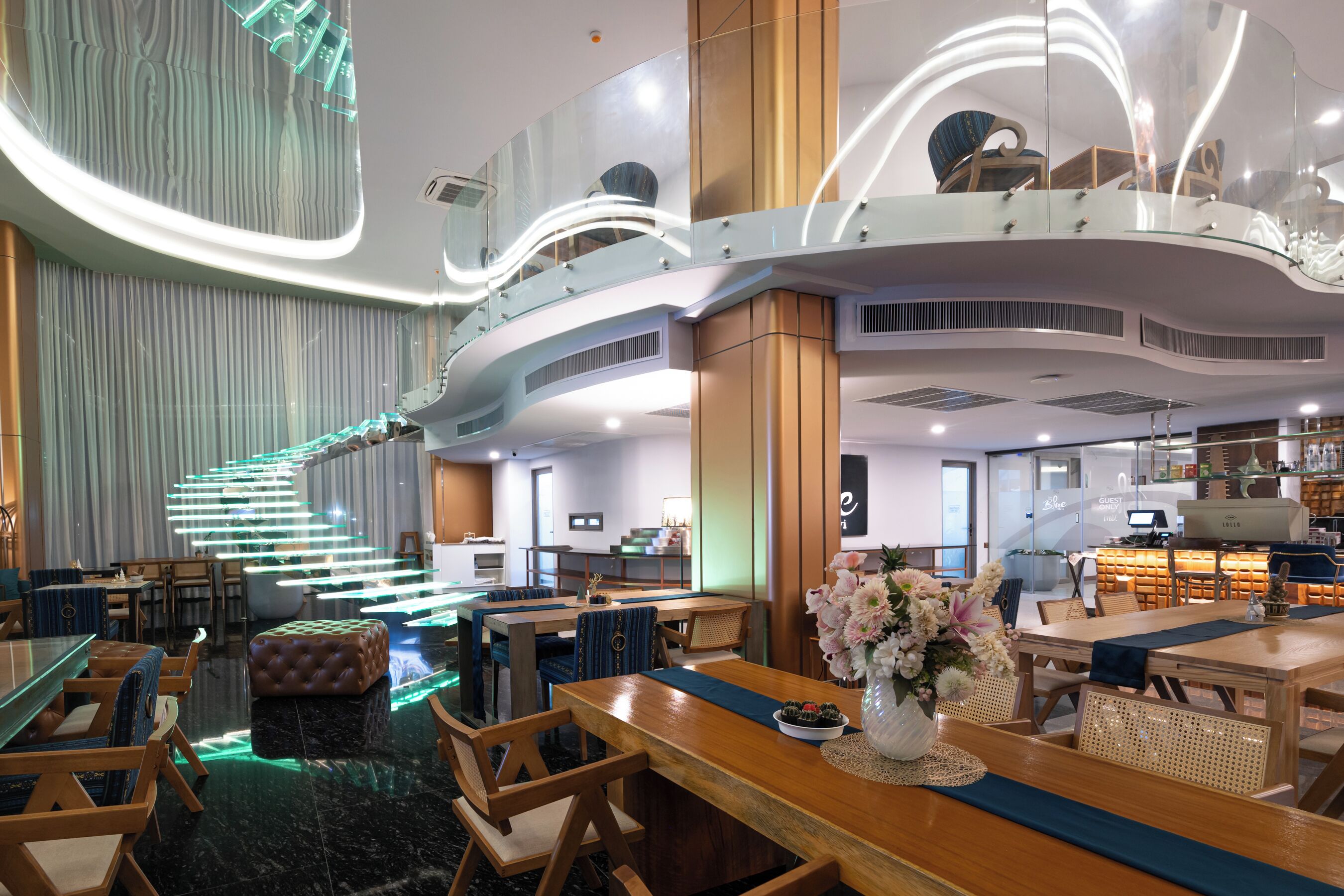 A modern hotel lobby with a curved staircase, seating areas, and a reception desk.