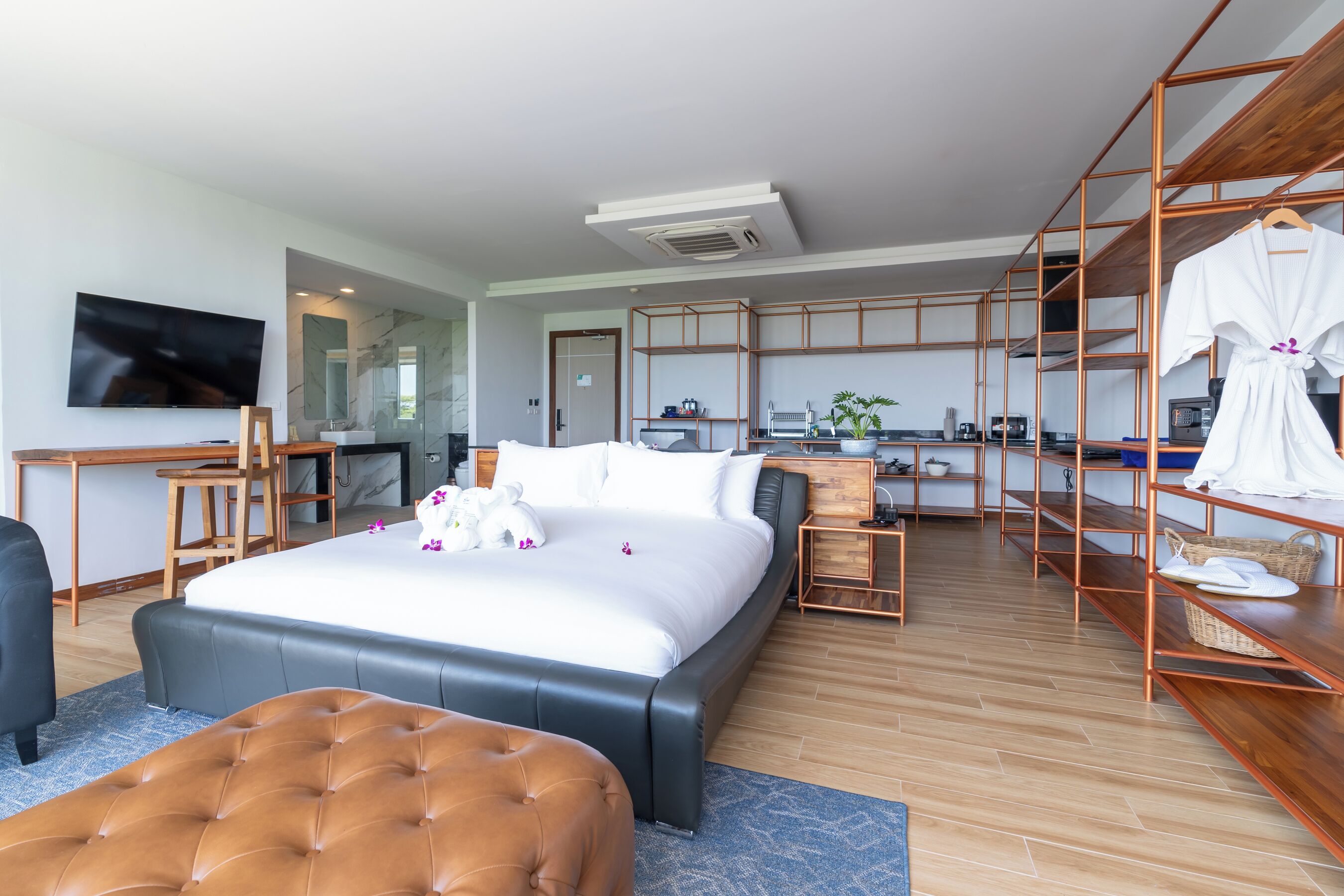 A modern hotel room with a large bed, a desk, a TV, and a kitchenette.