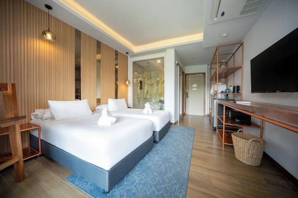 A hotel room with a large bed, a desk, a television, and a bathroom visible through a glass door.