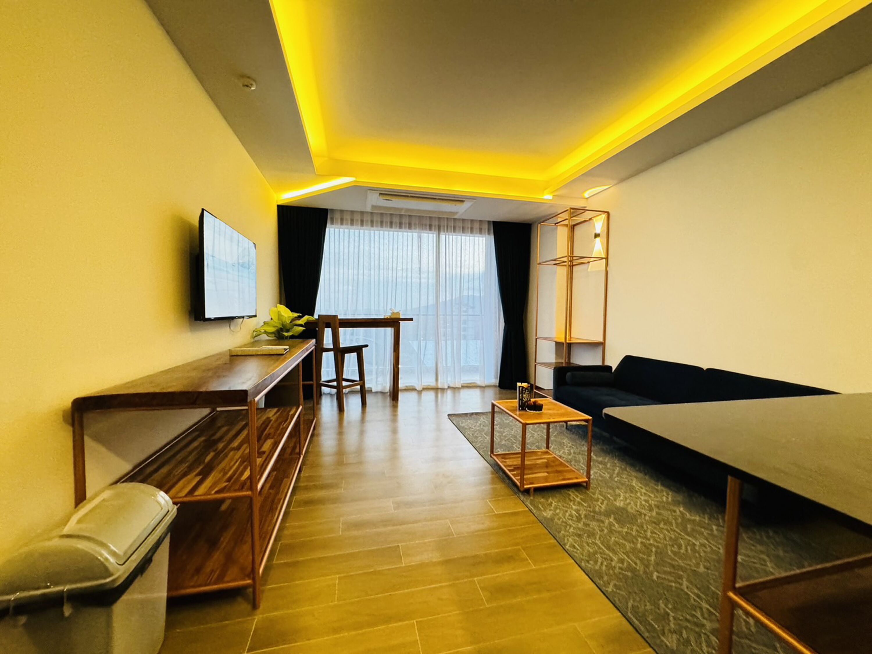 A modern living room with a sofa, a dining table, and a TV mounted on the wall.