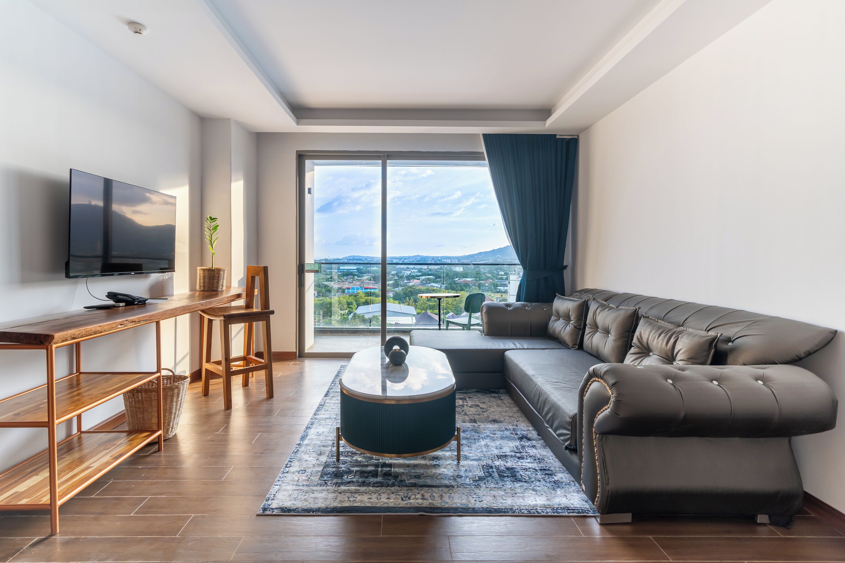 A modern living room with a large window, a flat-screen TV, a sofa, a coffee table, and a wooden side table.