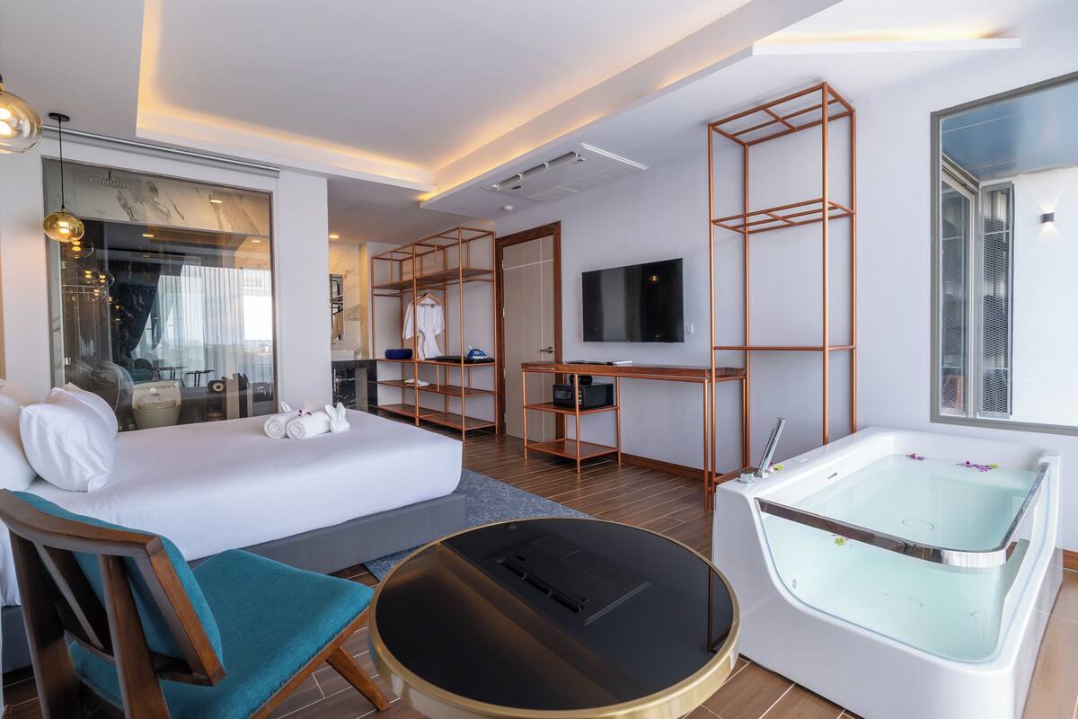 A modern hotel room with a bed, a round coffee table, a bathtub, a desk, and a TV.