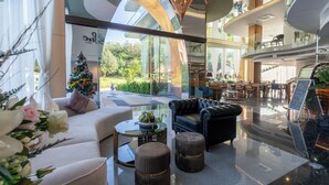 A modern hotel lobby with a glass wall, a Christmas tree, comfortable seating, and a view of the outdoors. - The Blue Mavi Hotel (Chalong)