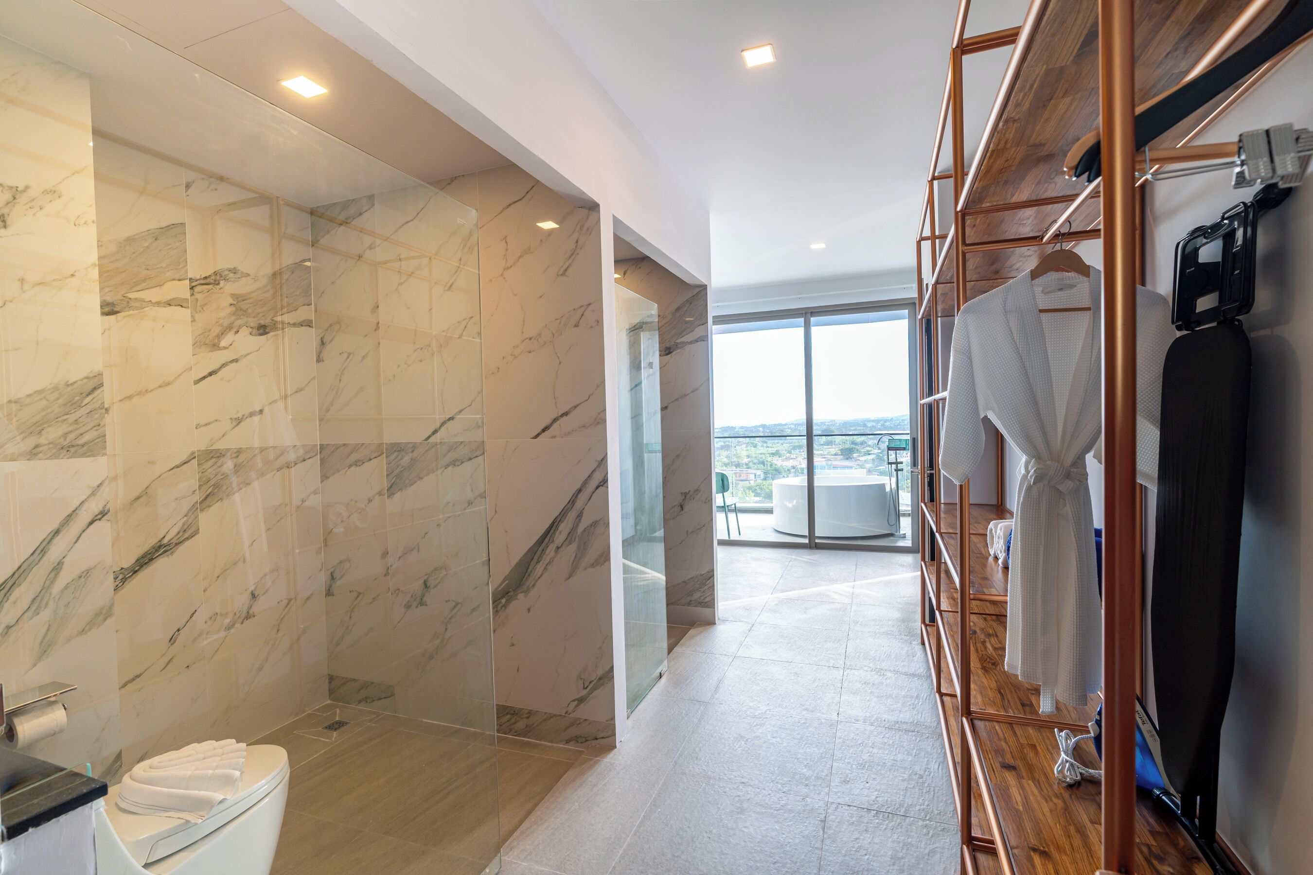 Ein modernes Badezimmer mit Marmorwänden, einer Duschkabine aus Glas und einem Holzwaschtisch mit Bademantelhalter.