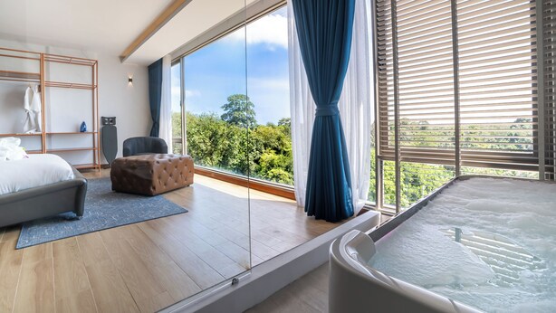 A modern bedroom with a large window, a bathtub, a sofa, and a wooden floor. - The Blue Mavi Hotel (Chalong)