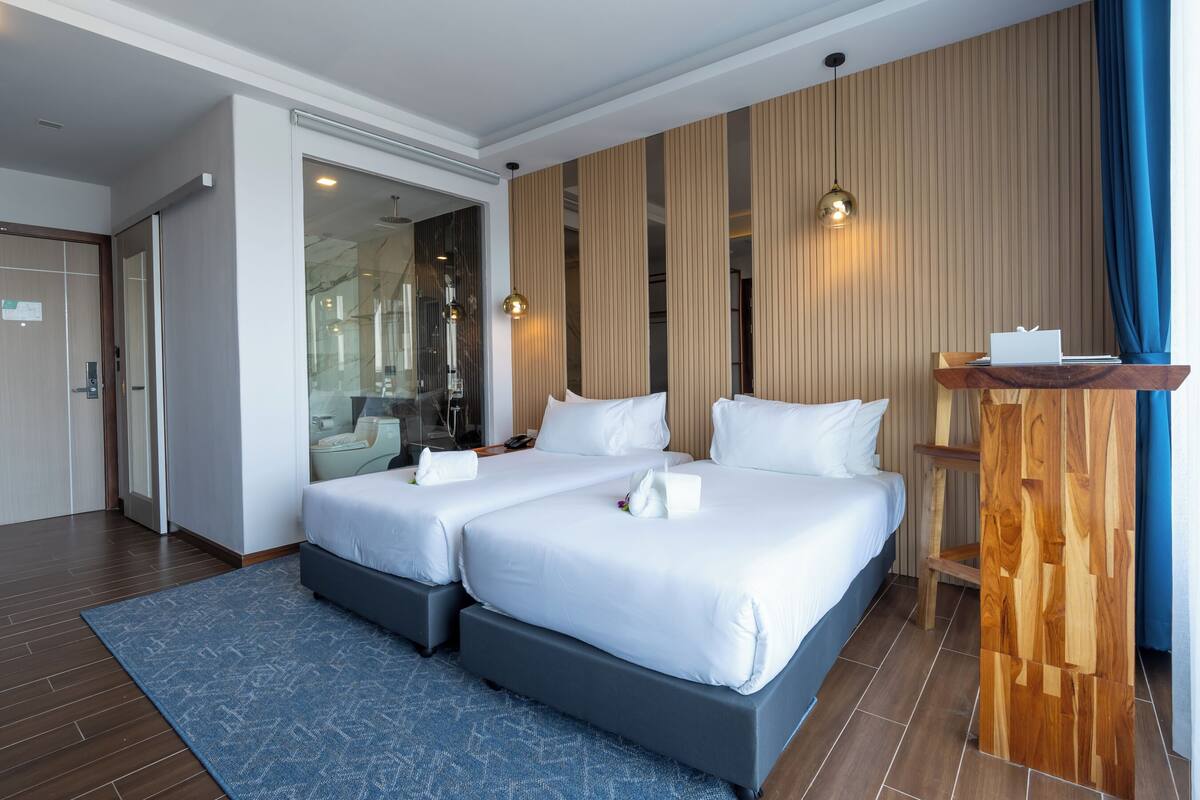 A hotel room with two beds, a wooden accent wall, a blue rug, and a wooden shelf with a laptop.