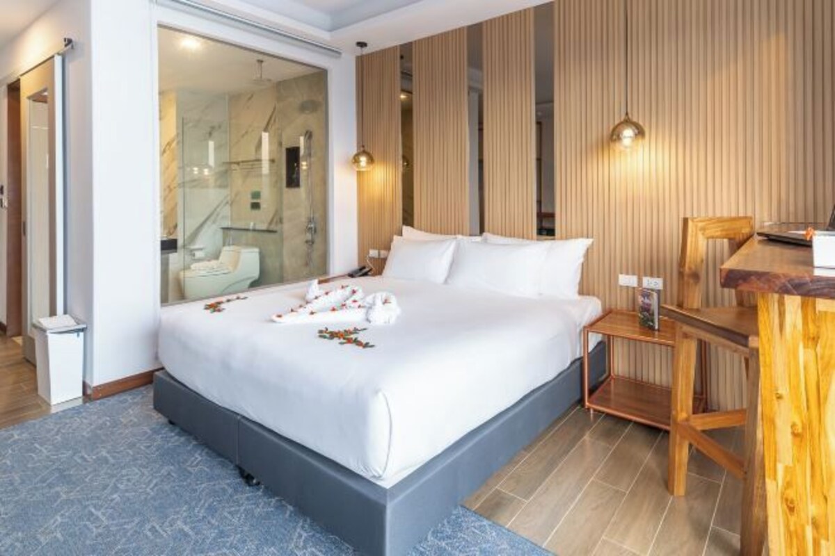 A modern hotel room with a large bed, a wooden desk, and a glass shower area.