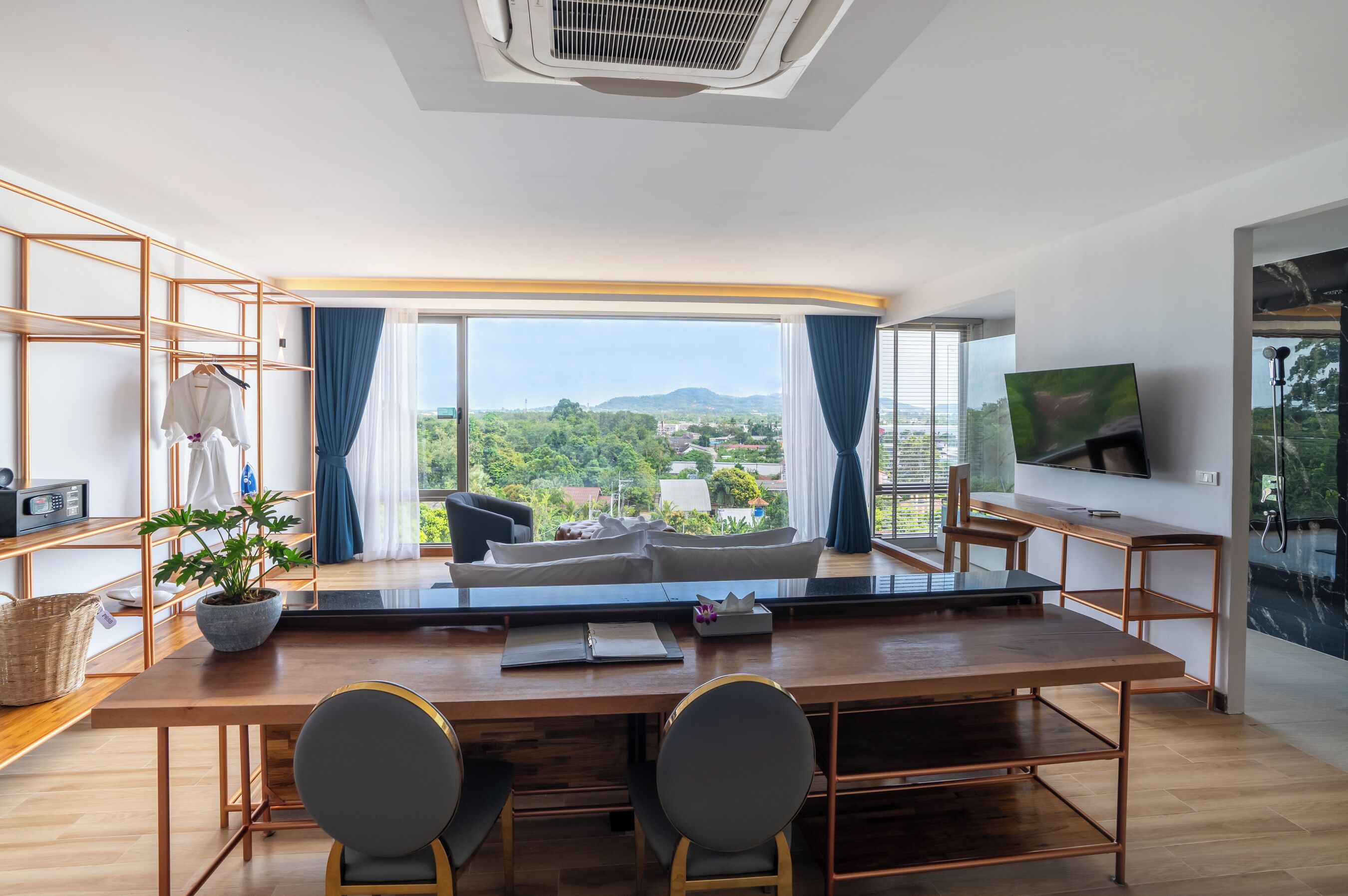 A modern room with a large window, a wooden dining table, two chairs, a sofa, a TV, and a plant.