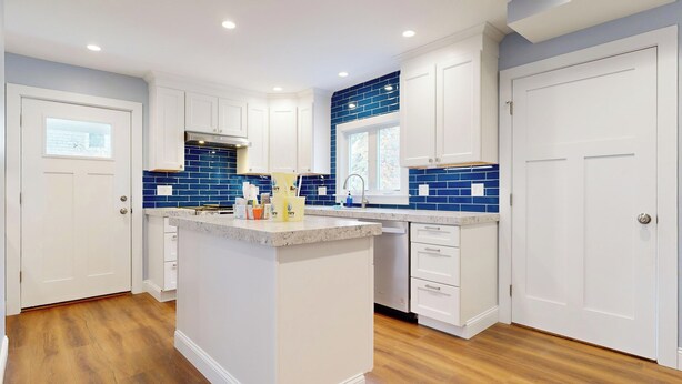A modern kitchen with white cabinetry, a central island, and blue-tiled backsplash.
