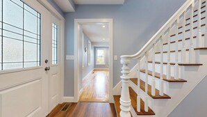 A hallway with a wooden floor, a white door with a frosted glass window, and a white staircase with wooden steps.