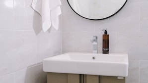 A bathroom with a white sink, a round mirror, and a towel hanging on the wall. - Raya Hotel Krabi (Krabi)