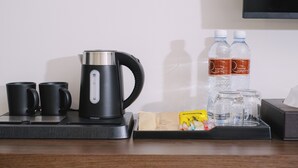 A coffee maker, two black mugs, two bottles of water, and a tray with a tissue box and some snacks on a wooden table. - Raya Hotel Krabi (Krabi)