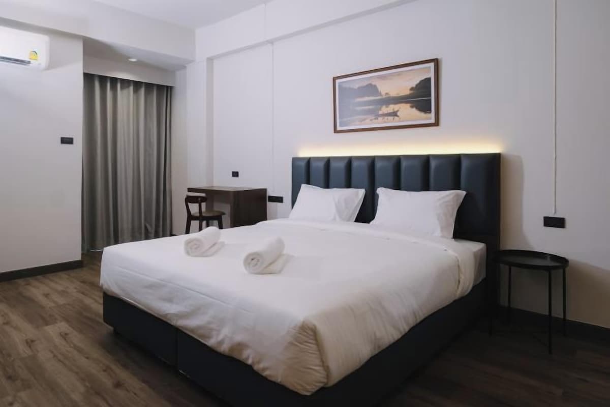 A hotel room with a large bed, a desk, a chair, and a painting on the wall.