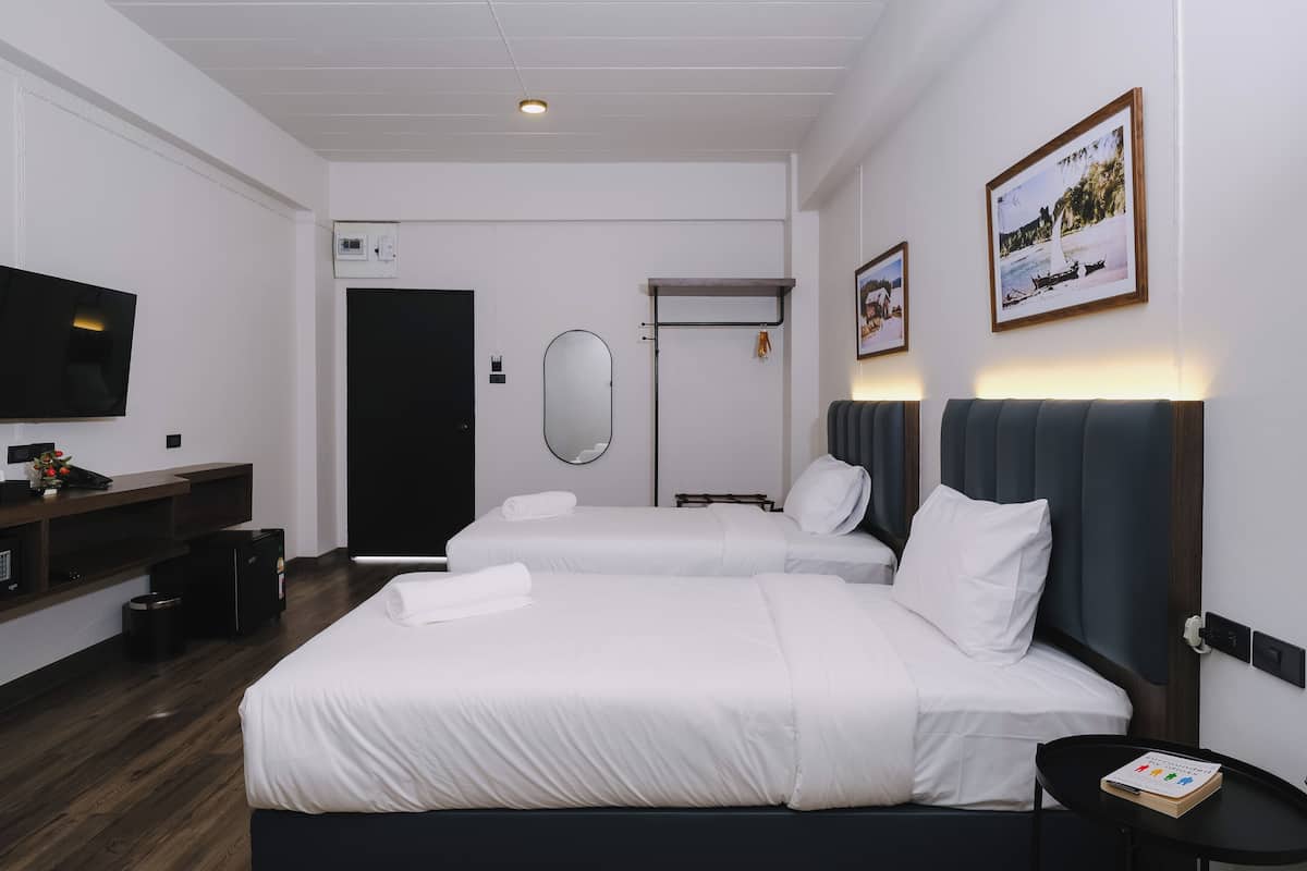 Une chambre d’hôtel avec deux lits, un téléviseur à écran plat, une petite table et un tableau encadré au mur.