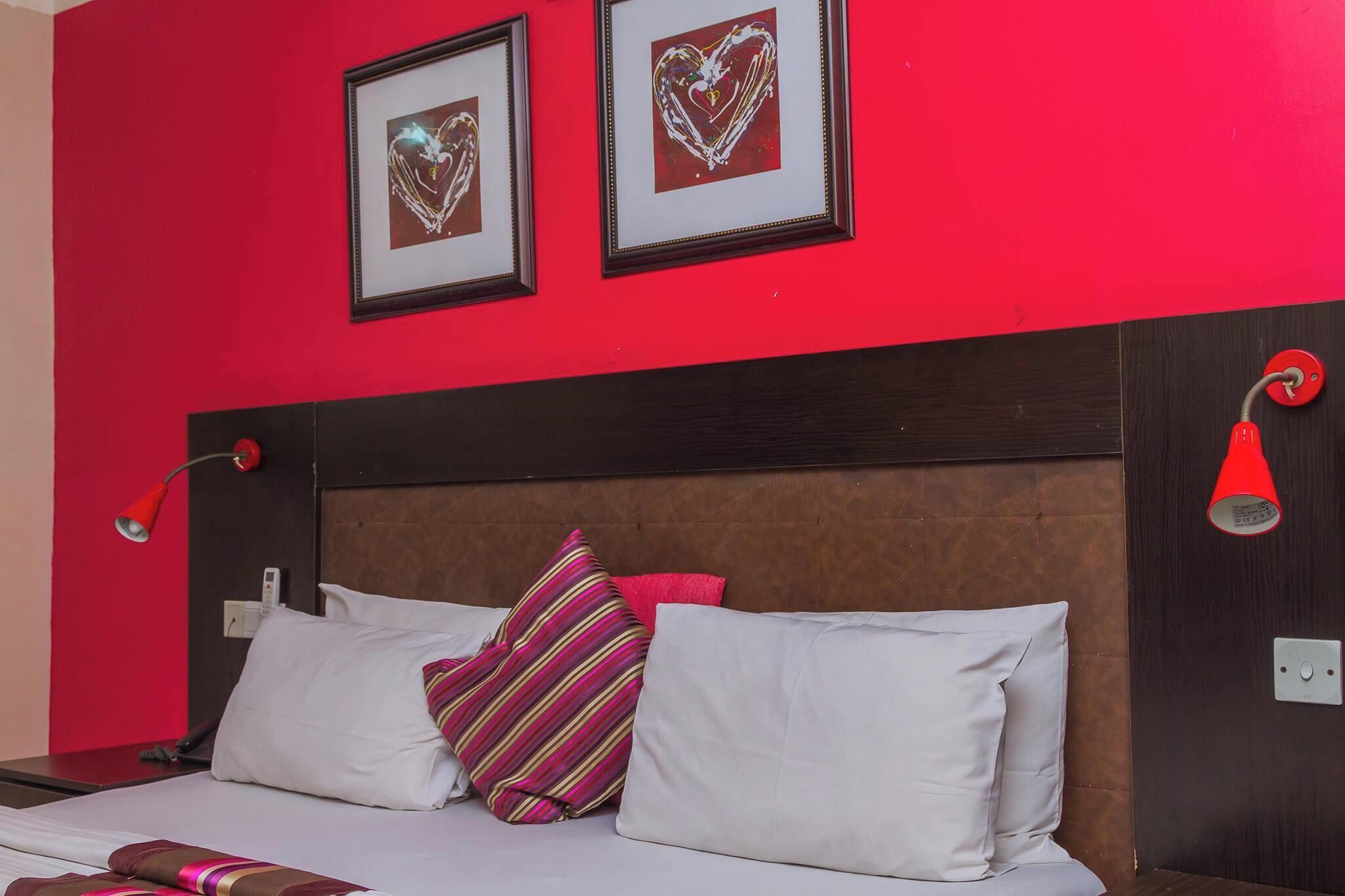 A hotel room with a red wall, a wooden headboard, and a bed with white and striped pillows.
