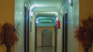 A hallway with a mirrored floor, two potted plants on either side, and a fire extinguisher on the wall. - The Grill House & Suites Asokoro Abuja (Abuja)