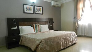 A neatly made bed with a patterned bedspread, a dark headboard, and two framed pictures on the wall. - The Grill House & Suites Asokoro Abuja (Abuja)