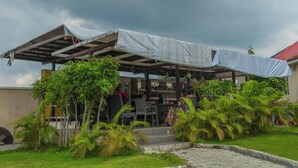 An outdoor seating area with a covered structure, surrounded by greenery and palm trees. - The Grill House & Suites Asokoro Abuja (Abuja)