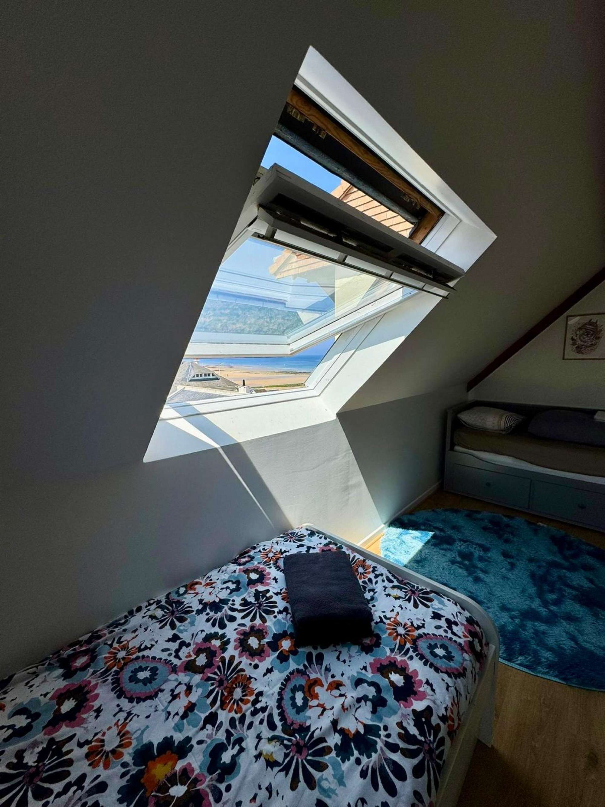 A small bedroom with a skylight, a bed with a floral bedspread, and a blue rug.