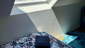 Una habitació amb un òculi, un llit amb una colcha floral i una catifes blava.