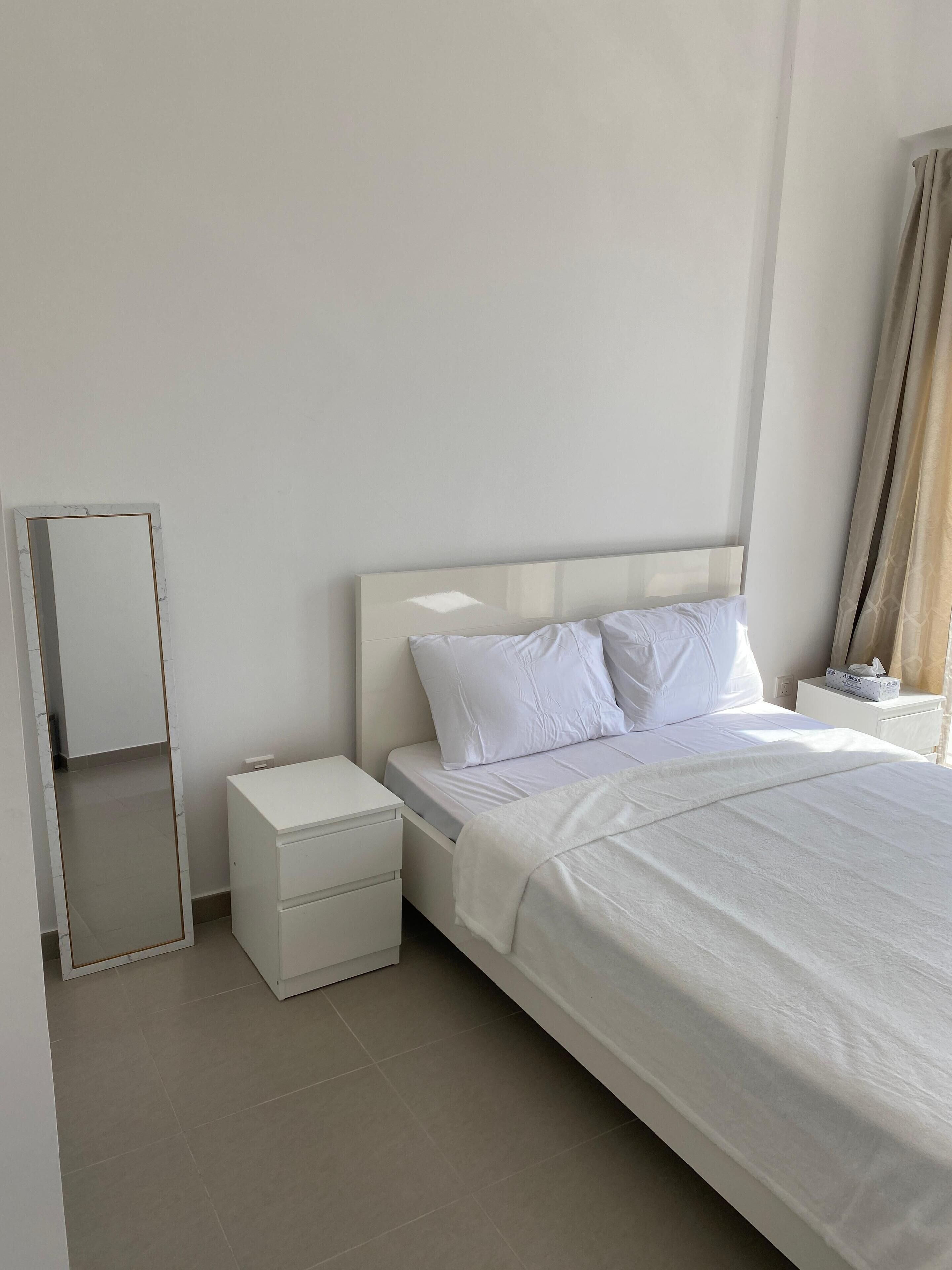 Een minimalistisch hotelkamer met een groot bed, een nachtkastje en een spiegel.