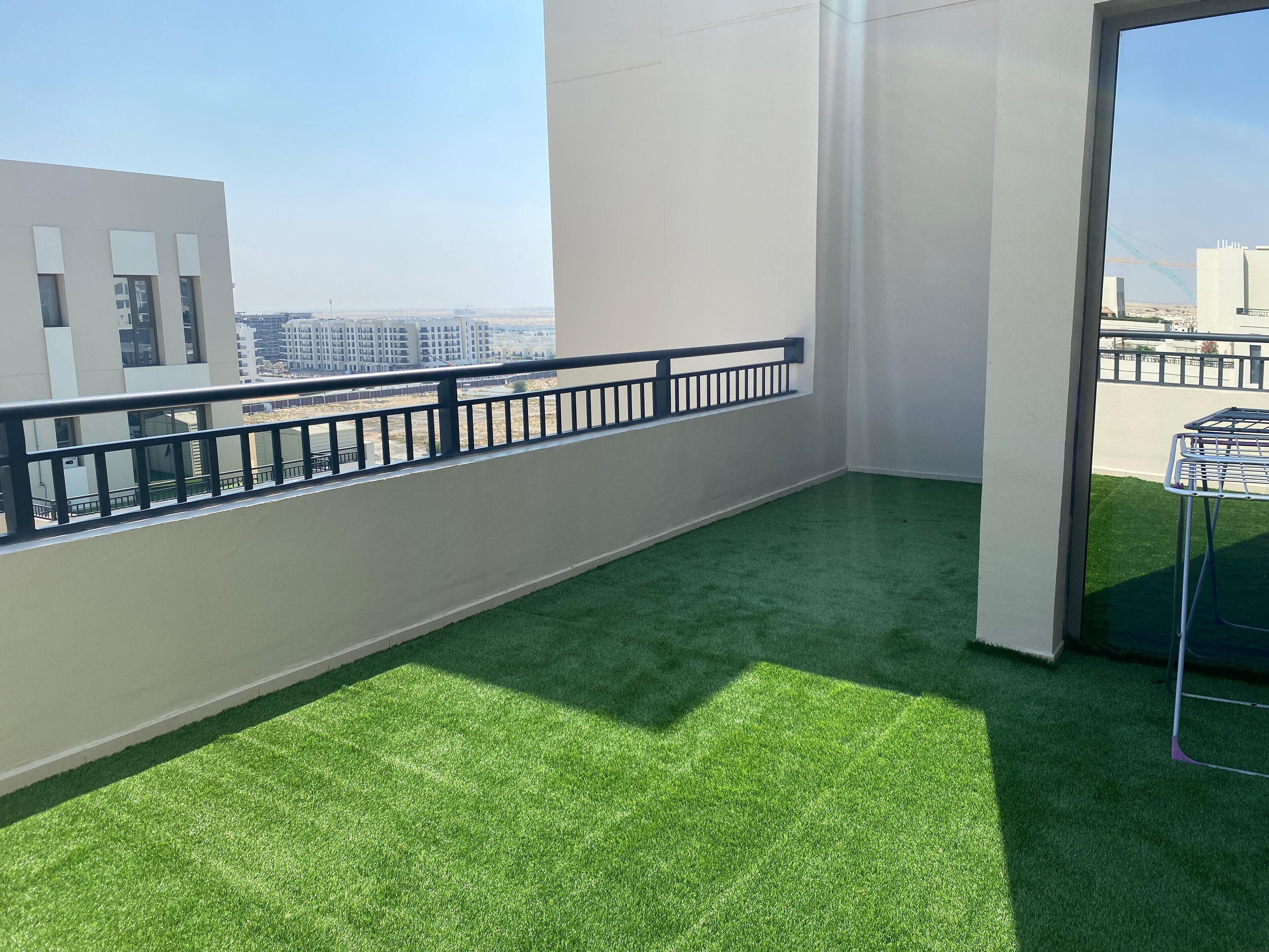 Un balcó amb gespa artificial, una barana metàl·lica i vista a edificis allunyats.