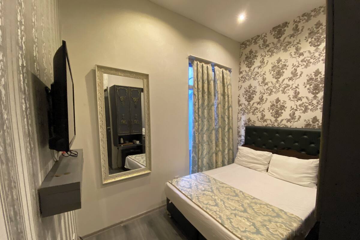 A bedroom with a bed, a mirror, a wardrobe, and a television.