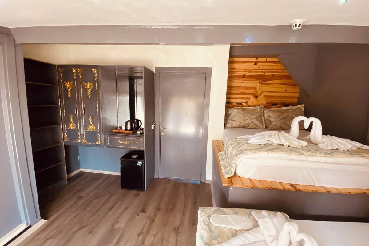 A modern hotel room with a wooden headboard, a bed with white linens, a bedside table, and a wardrobe with gold accents.