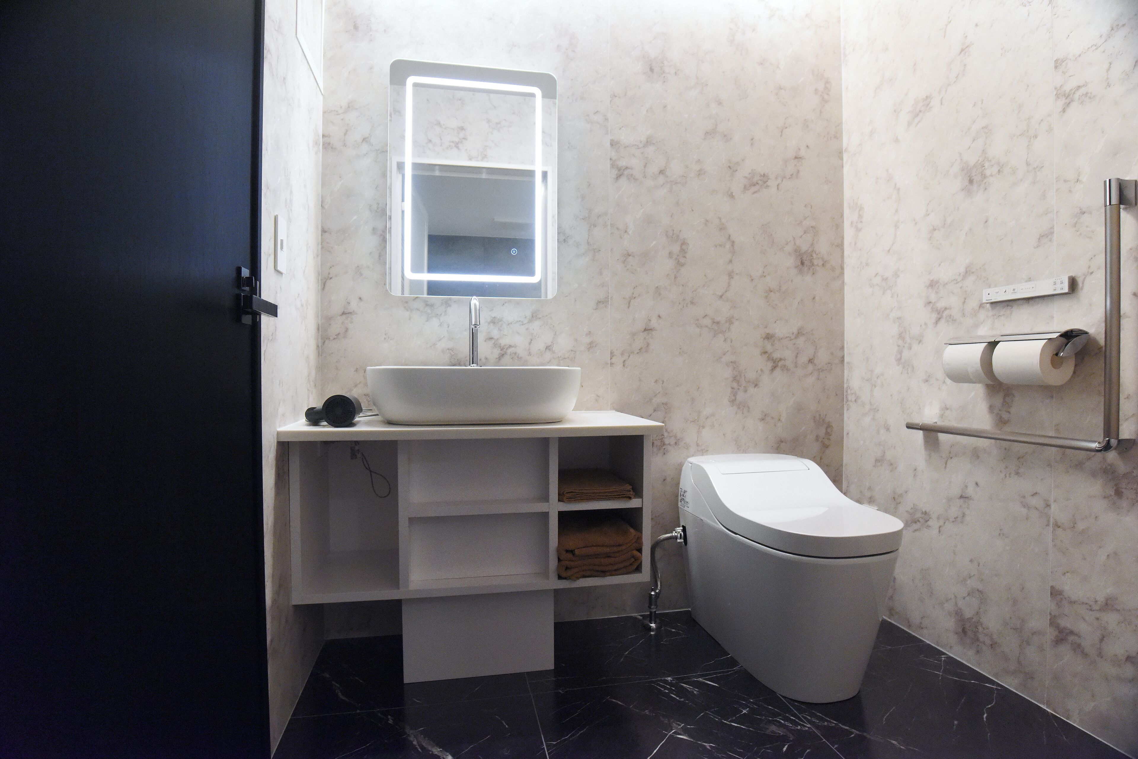 A modern bathroom with a white sink, a toilet, and a marble-tiled wall.