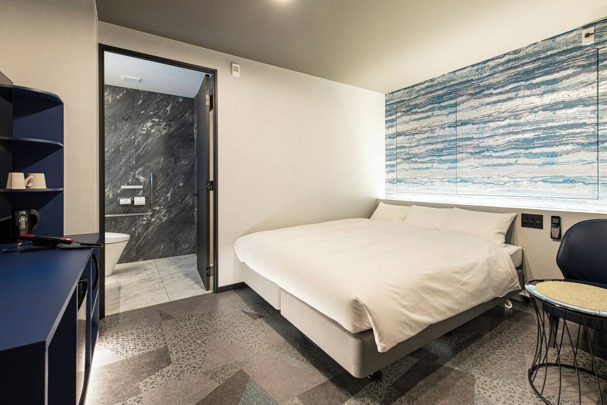 Une chambre d’hôtel moderne, équipée d’un lit, d’un bureau, d’une chaise et d’un grand tableau abstrait accroché au mur.