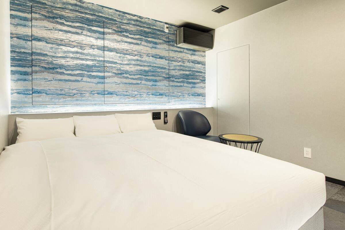 Une chambre d’hôtel avec un grand lit, une chaise, une petite table et un climatiseur fixé au mur.