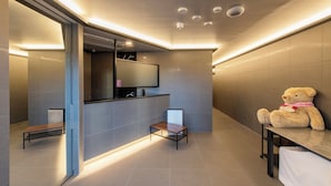 A modern bathroom with a large mirror, a small table, and a teddy bear on a bench.