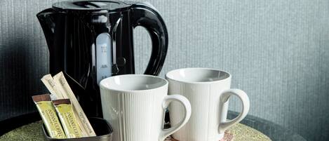 A black coffee maker, two white mugs, and instant coffee packets on a table.