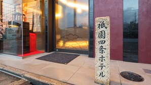 A stone pillar with Japanese characters, a glass door entrance, a red bench, and a metal grate on the sidewalk.