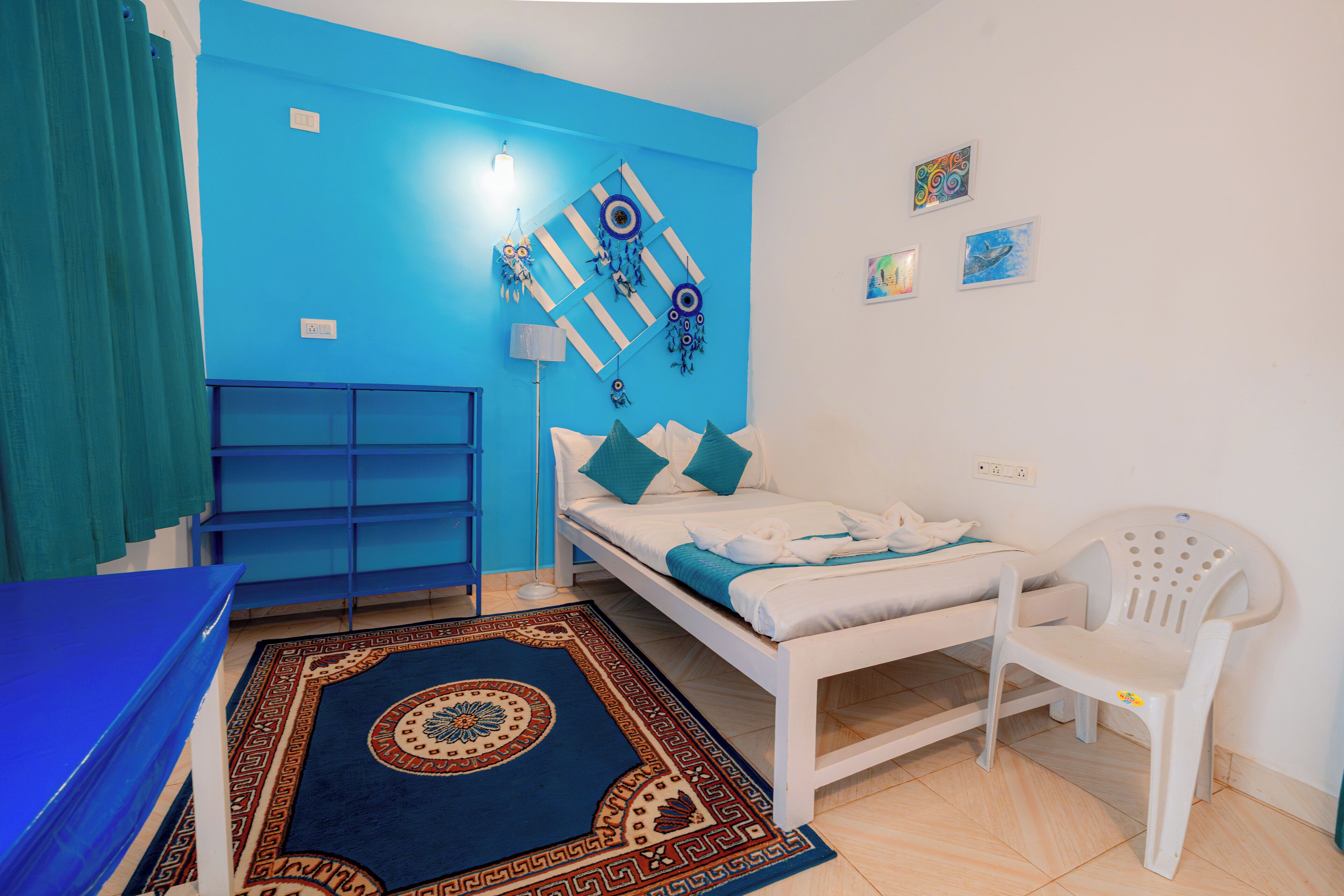 A room with a bed, a chair, a blue wall, and a patterned rug.