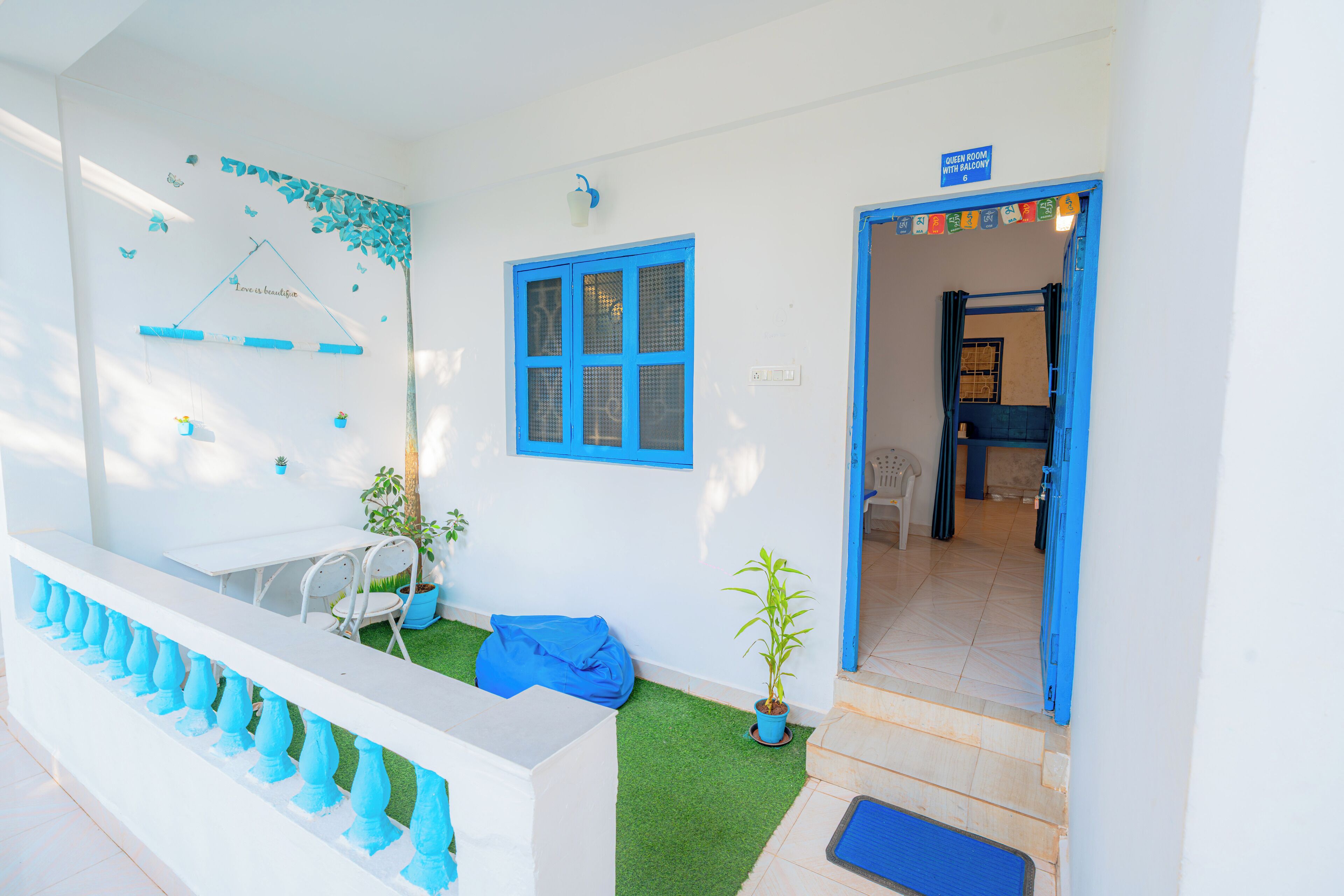 A white building with blue accents, a small garden area with artificial grass, a blue door, and a staircase leading to an upper level.