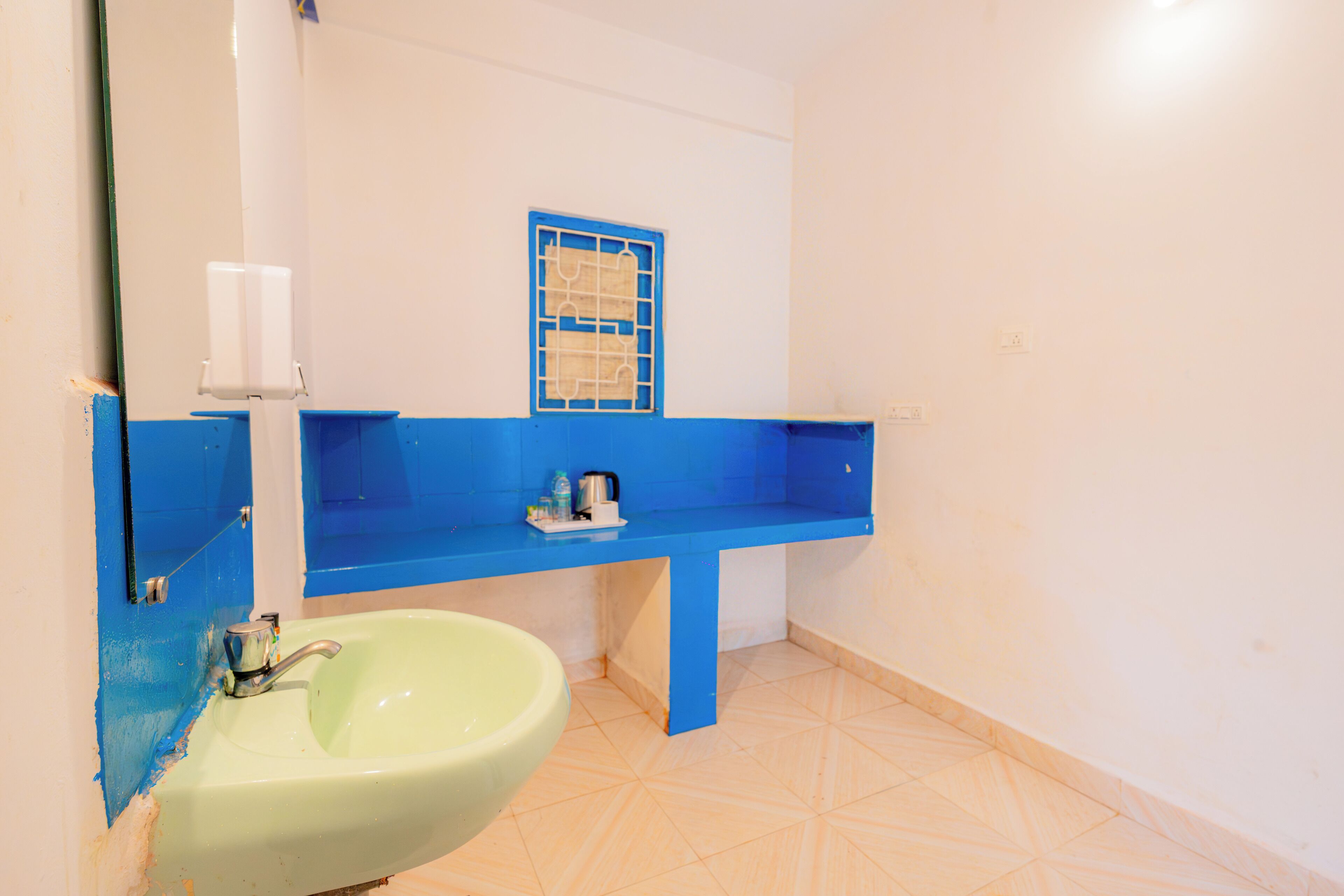 Une salle de bain avec un lavabo vert, un meuble-lavabo bleu et une fenêtre à motifs géométriques.