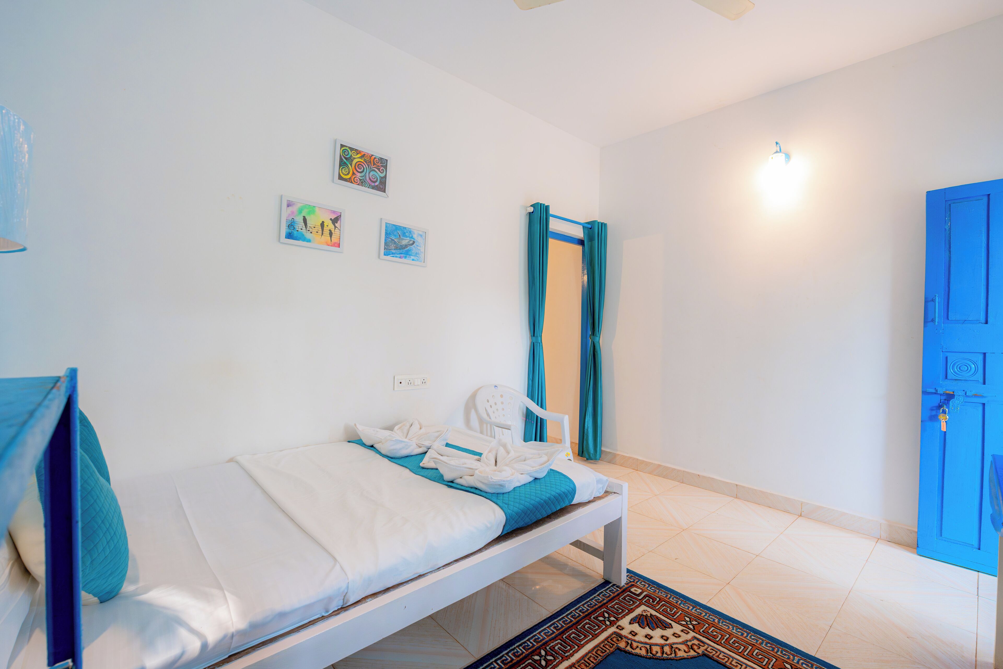 Un dormitorio con una cama, una puerta azul y una pared blanca decorada con obras de arte.